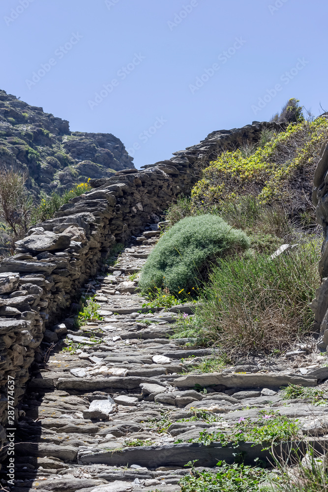 Narrow path with stone stairs in the mountains (Cyclades, Andros Island, Greece)