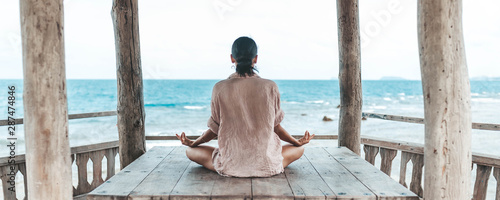 young woman meditating in a yoga pose at the beach