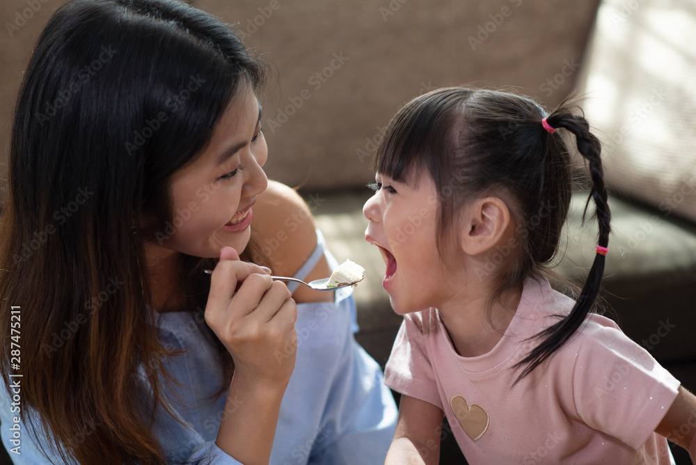 Young Asian woman feeding her younger sister with spoon of tasty cake Young Asian woman feeding her younger sister with spoon of tasty cake