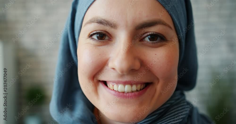 Slow motion close-up portrait of beautiful Muslim girl in hijab smiling in office looking at camera with joyful face. Attractive people, workplace and happiness concept. Slow motion close-up portrait of beautiful Muslim girl in hijab smiling in office looking at camera with joyful face. Attractive people, workplace and happiness concept.