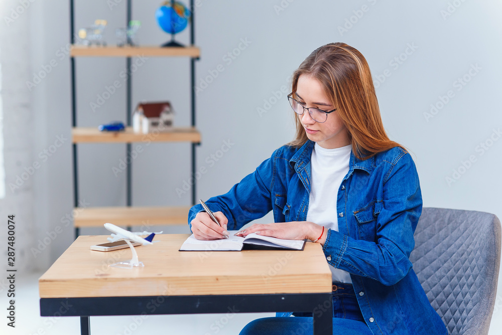 Beautiful young woman in office wearing denim clothes, make some notes on note book.
