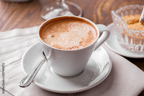 cup of coffee close-up with spoon, saucer, brown sugar bowl and linen napkin on wooden table