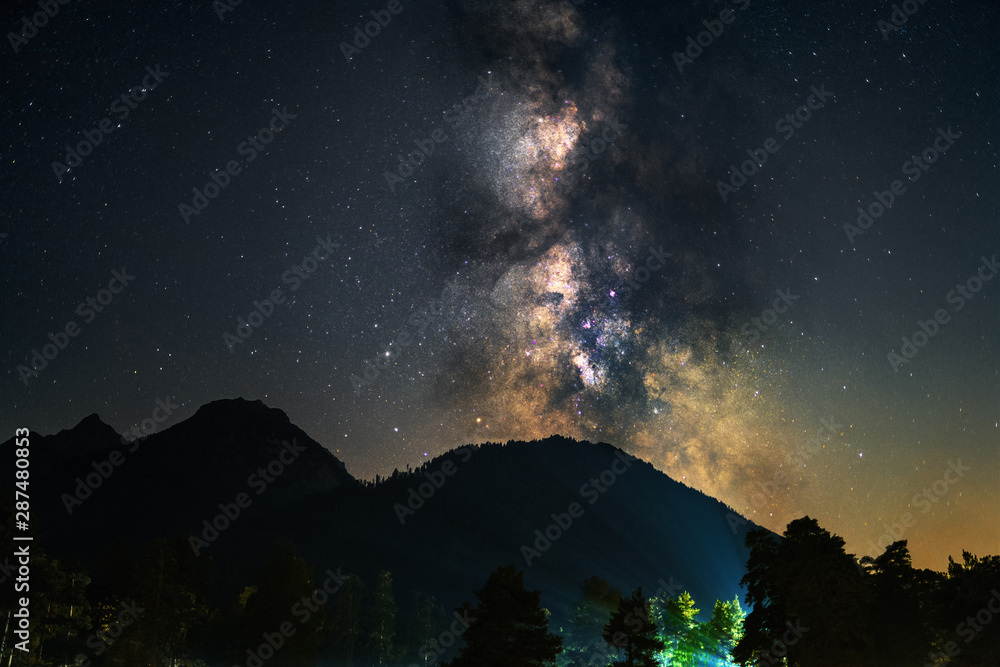 Milky Way galaxy in Universe astrophotography. Silhouettes of mountains and trees. Stars and nebula at night sky landscape