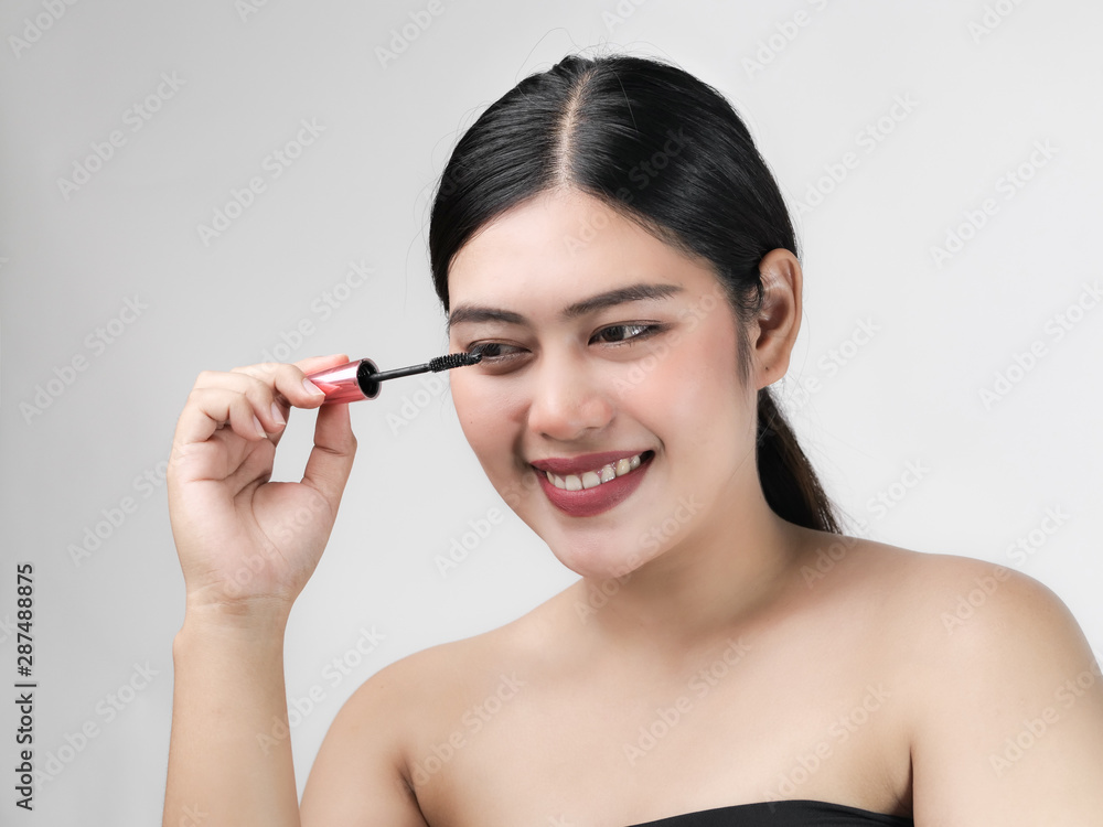 Close-up portrait of nice lovely cute sweet attractive cheerful positive Asian woman holding in hands applying trendy black mascara isolated over gray background. Close-up portrait of nice lovely cute sweet attractive cheerful positive Asian woman holding in hands applying trendy black mascara isolated over gray background.