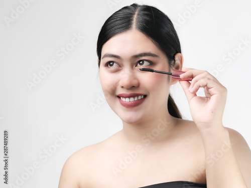 Close-up portrait of nice lovely cute sweet attractive cheerful positive Asian woman holding in hands applying trendy black mascara isolated over gray background.