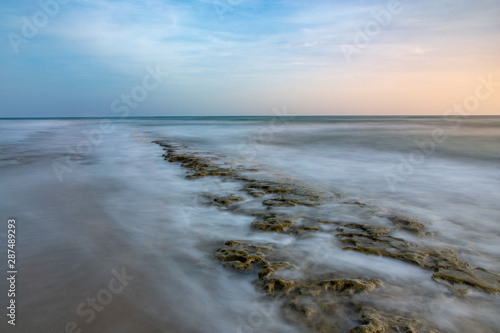Seascape horizon with rocks in the water and ocean waves at sunrise on Cabarete beach, Dominican Republic