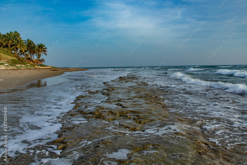 Seascape horizon with rocks in the water and ocean waves at sunrise on Cabarete beach, Dominican Republic