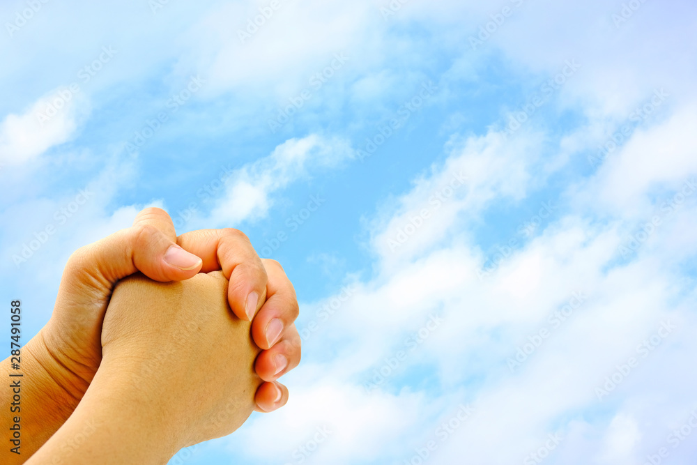 Prayer hands to God from bottom left of the frame with blue sky as background. Prayer hands to God from bottom left of the frame with blue sky as background.
