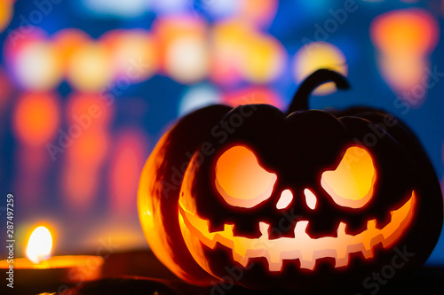 Spooky pumpkin head jack o' lantern glowing with a burning candle. Halloween background, bokeh