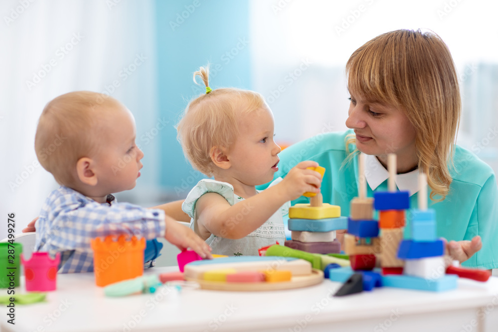 Nursery teacher looking after children in daycare. Little kids toddlers play together with developmental toys. Babies with caregiver in creche Nursery teacher looking after children in daycare. Little kids toddlers play together with developmental toys. Babies with caregiver in creche