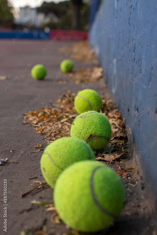 Pelotas de tenis y raqueta en cancha profesional en el piso con fondo de ciudad y red de la cancha