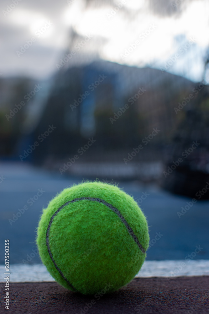 Pelotas de tenis y raqueta en cancha profesional en el piso con fondo de ciudad y red de la cancha