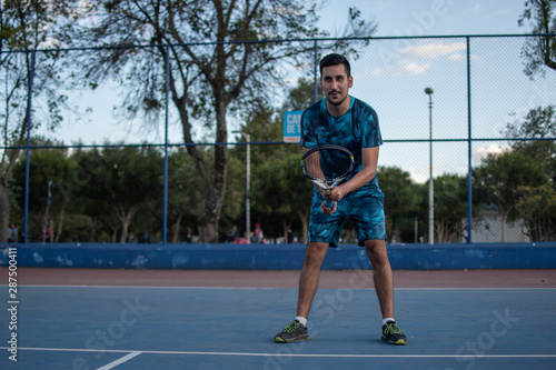 Hombre adulto latino con barba de camiseta azul en pantaloneta jugando tenis  con amigo en cancha profesional  hispano