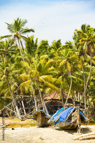 Stunning view of a beach with a wooden boat in front of a fishing village surrounded by beautiful palm trees. Varkala, Kerala, India.