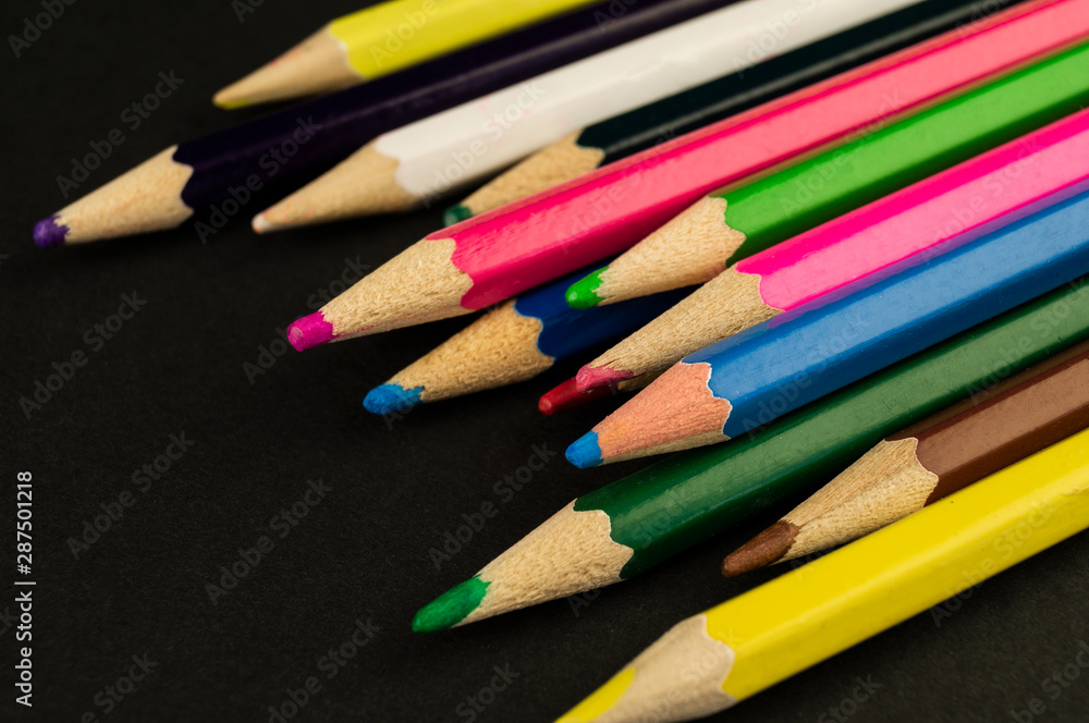 Many colorful pencils lie on a black background paper