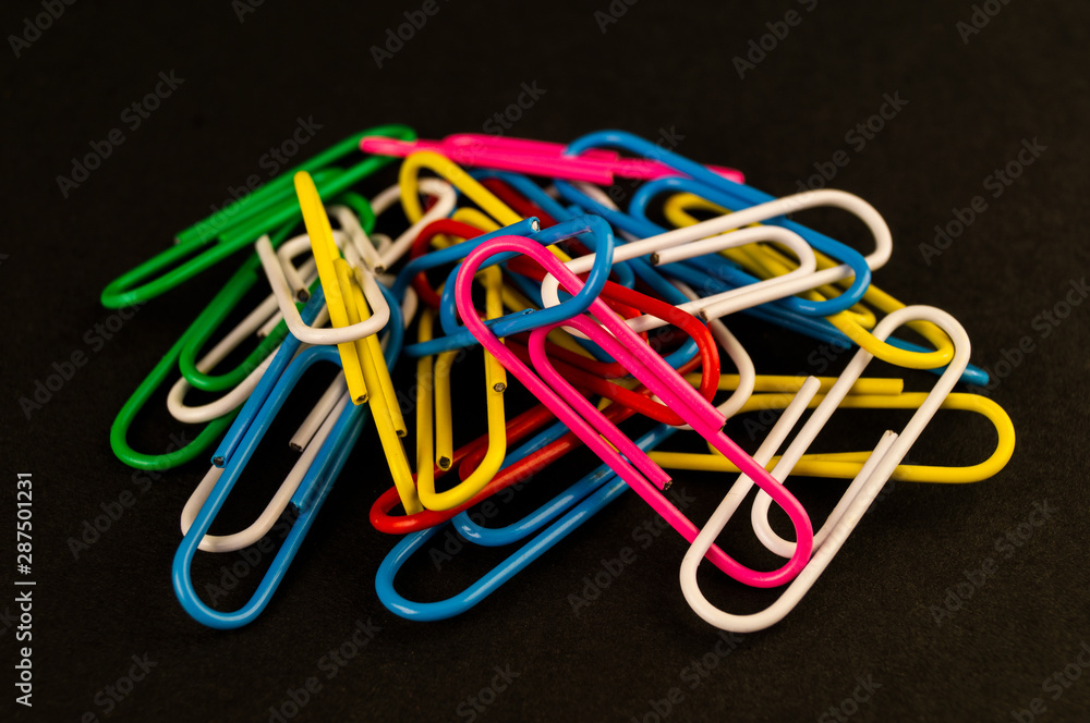 Many colorful paper clips lie on a black background paper Many colorful paper clips lie on a black background paper