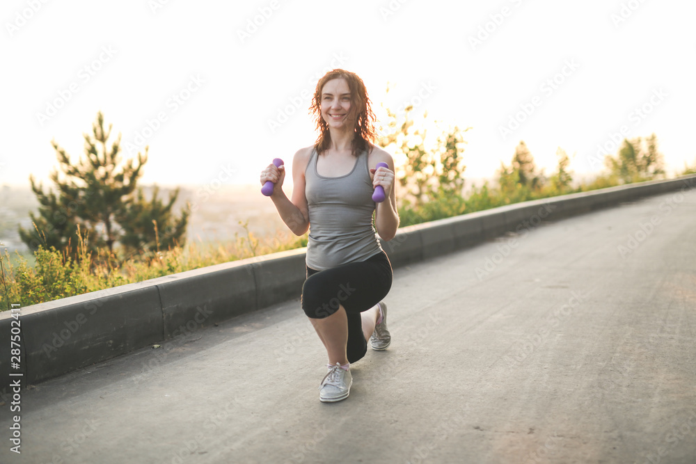 woman with dumbbells goes in sports in park