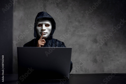 Hacker wearing a white mask in front of his computer. hacker hacks network, Space for text. photo