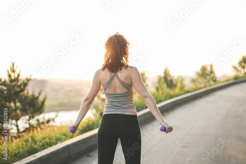 woman with dumbbells goes in sports in park