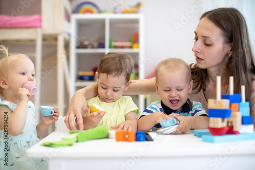 Kids toddlers play with plastic tableware, Educator looks after nursery babies