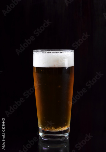 Beer with foam in a tall glass against black background