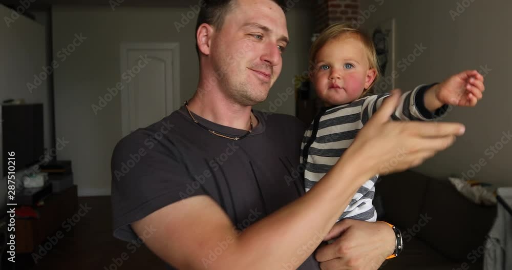 Irritated toddler with eyebrows frowned lips pursed in fathers hands looking at camera Irritated toddler with eyebrows frowned lips pursed in fathers hands looking at camera