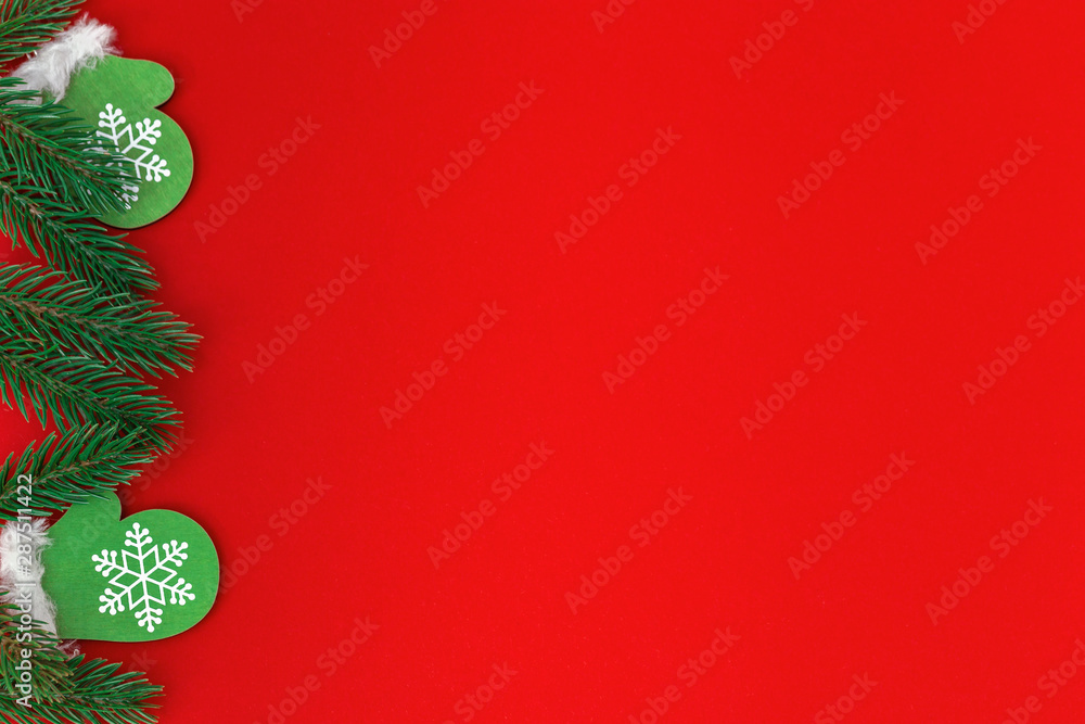 Small wooden christmas toy Green mittens with pine branches on red paper background with copy space. Christmas greeting card. Small wooden christmas toy Green mittens with pine branches on red paper background with copy space. Christmas greeting card.