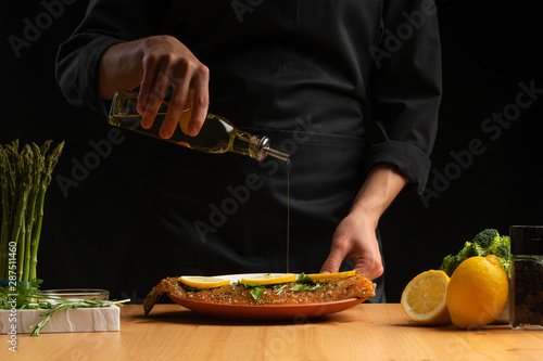 Chef oiling seafood, red salmon or trout fish, freezing in motion, Asian cuisine, recipe book, on black background. Preparing tasty and healthy food. Horizontal photo.