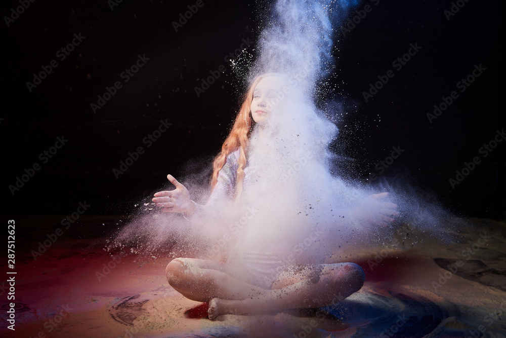 Fototapeta premium Beautiful teen girl with long blonde curly hair in a dark room with colored lights and clouds of flour