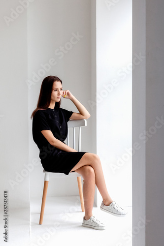 Young girl in black dress is sitting on a chair in the room