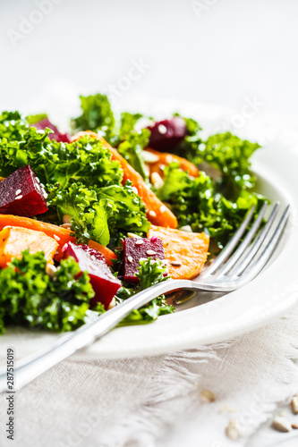 Kale salad with baked vegetables in white plate.