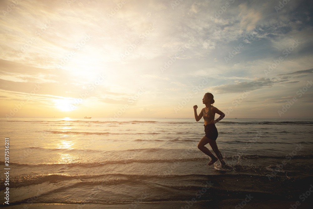 Silhouette of an athletic woman running on the beach during sunset time