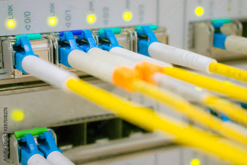 Optical fiber wires are connected to high-speed interfaces. Lots of yellow internet cables. Front panel of the central router with a set of optical links is in the server room of the data center.