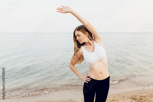 Fototapeta Naklejka Na Ścianę i Meble -  beautiful young sports fitness woman outdoors on the beach in the morning doing stretching exercises