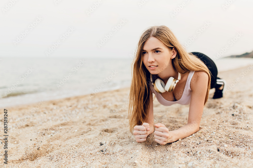 young girl in sportswear in the morning outdoors on the beach making a plank young girl in sportswear in the morning outdoors on the beach making a plank