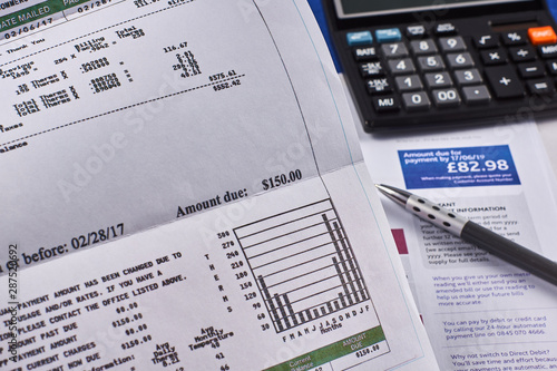 Comparison of utility bills in dollars and pounds. Utility bill sheets, calculator and pen. Close-up