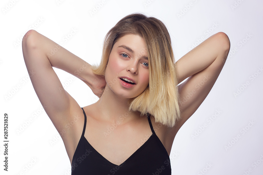Beautiful portrait of a young blonde woman with day makeup and shaved armpits. Girl stretches for camera on white background. Nice smile and clear skin. Cosmetology and spa Beautiful portrait of a young blonde woman with day makeup and shaved armpits. Girl stretches for camera on white background. Nice smile and clear skin. Cosmetology and spa
