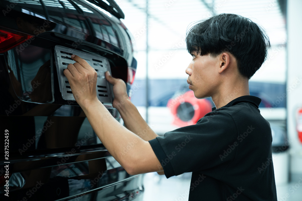 Asian man installing the licence plate of a car. Technician installing car plate. A car plate being install by Asian man. Car license plate black. licence holder adjusting on black vehicle. Asian man installing the licence plate of a car. Technician installing car plate. A car plate being install by Asian man. Car license plate black. licence holder adjusting on black vehicle.