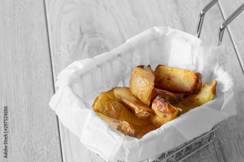 Potato wedges chips in a wire mesh serving basket with greaseproof paper.  Grey wood background photo