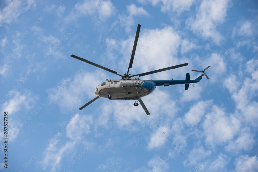 A white and blue helicopter flying in the sky - the cable hangs out of the helicopter A white and blue helicopter flying in the sky - the cable hangs out of the helicopter