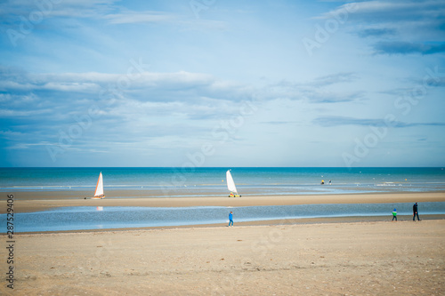 Two sand yachts racing on the beach on a sunny autumn day witt people walking on the beach