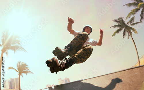 Rollerskater man is performing tricks in skatepark on sunset.