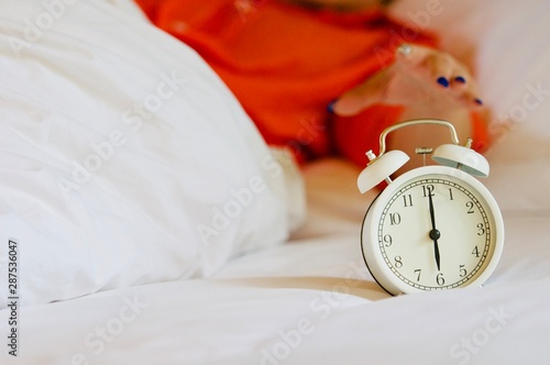 The woman's hand under the blanket reaches out for the alarm clock. Alarm clock that reminds the morning.