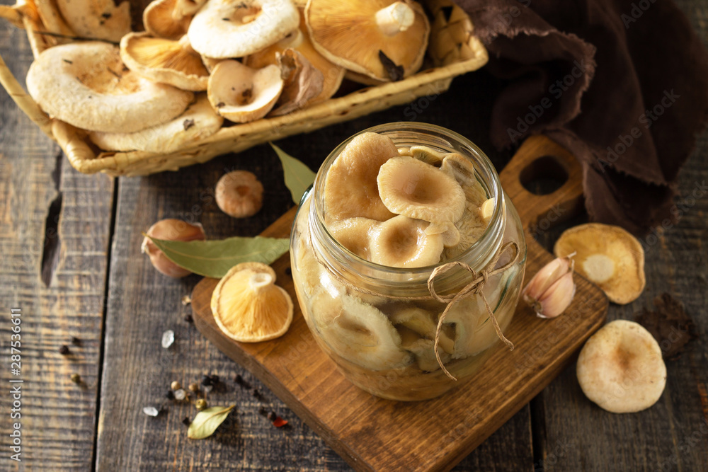 Fototapeta premium Mushroom preservation. Home preservation of products: glass jars with pickled mushrooms with spices on a rustic wooden table.