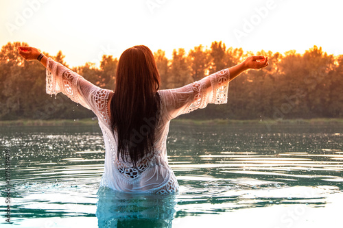 Frau in weißem Kleid steht in See, Sonnenuntergang photo