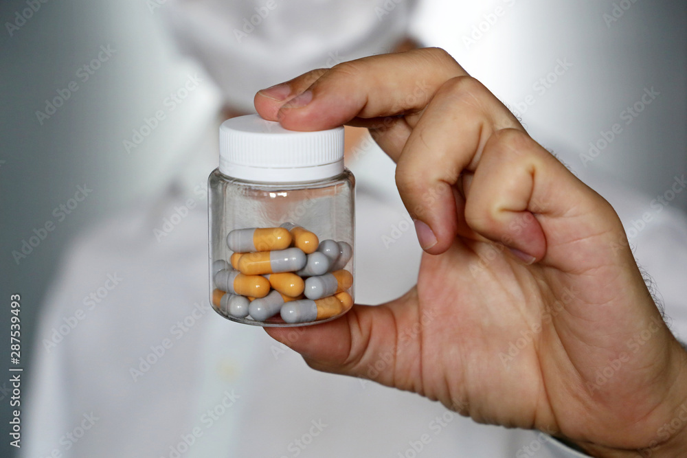 Doctor giving pills, physician in medical mask holding in hand bottle with capsules. Concept of dose of drugs, vitamins, pharmacy Doctor giving pills, physician in medical mask holding in hand bottle with capsules. Concept of dose of drugs, vitamins, pharmacy