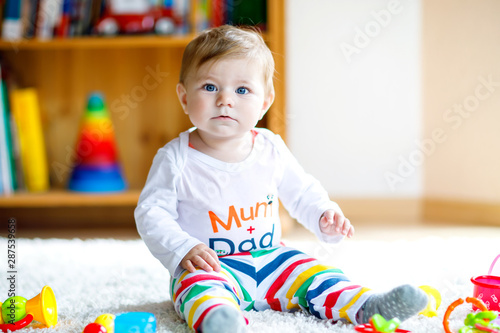 Adorable baby girl playing with educational toys in nursery. Happy healthy child having fun with colorful different toys at home. Baby development and first steps, learning to play and to grab.