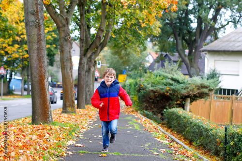 Happy little boy running on autumnal street after school. Kid happy about school vacations. Child with autumn fashion clothes wearing eye glasses