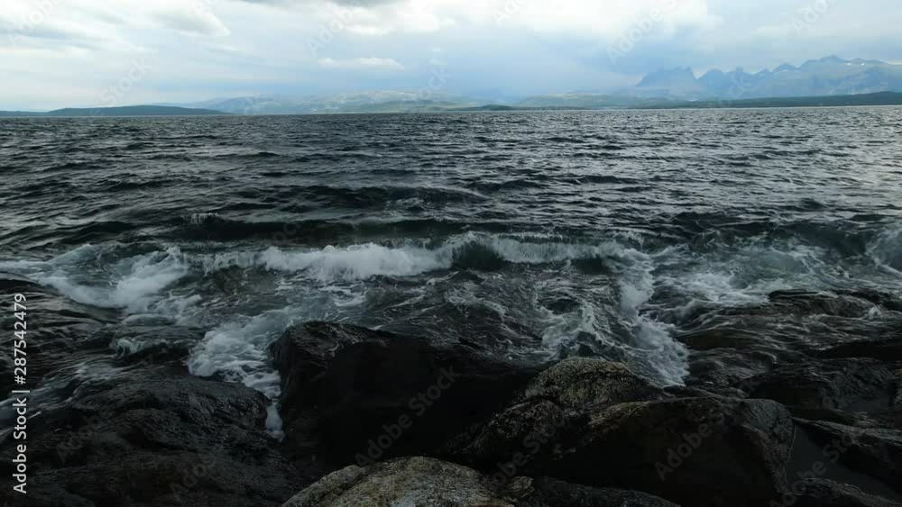 Dark waves breaking repeatedly, splashing on big rocks, on a gloomy, cloudy day at the sea. Moody shot of the rough ocean, negative sign or depression concept. Dark waves breaking repeatedly, splashing on big rocks, on a gloomy, cloudy day at the sea. Moody shot of the rough ocean, negative sign or depression concept.