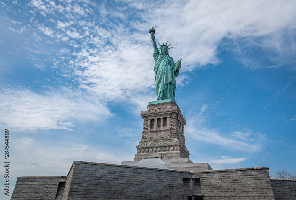 Shot of the Statue of Liberty in New York City, Usa. The shot is taken during a beautiful sunny day with a blue sky and white clouds in the background	